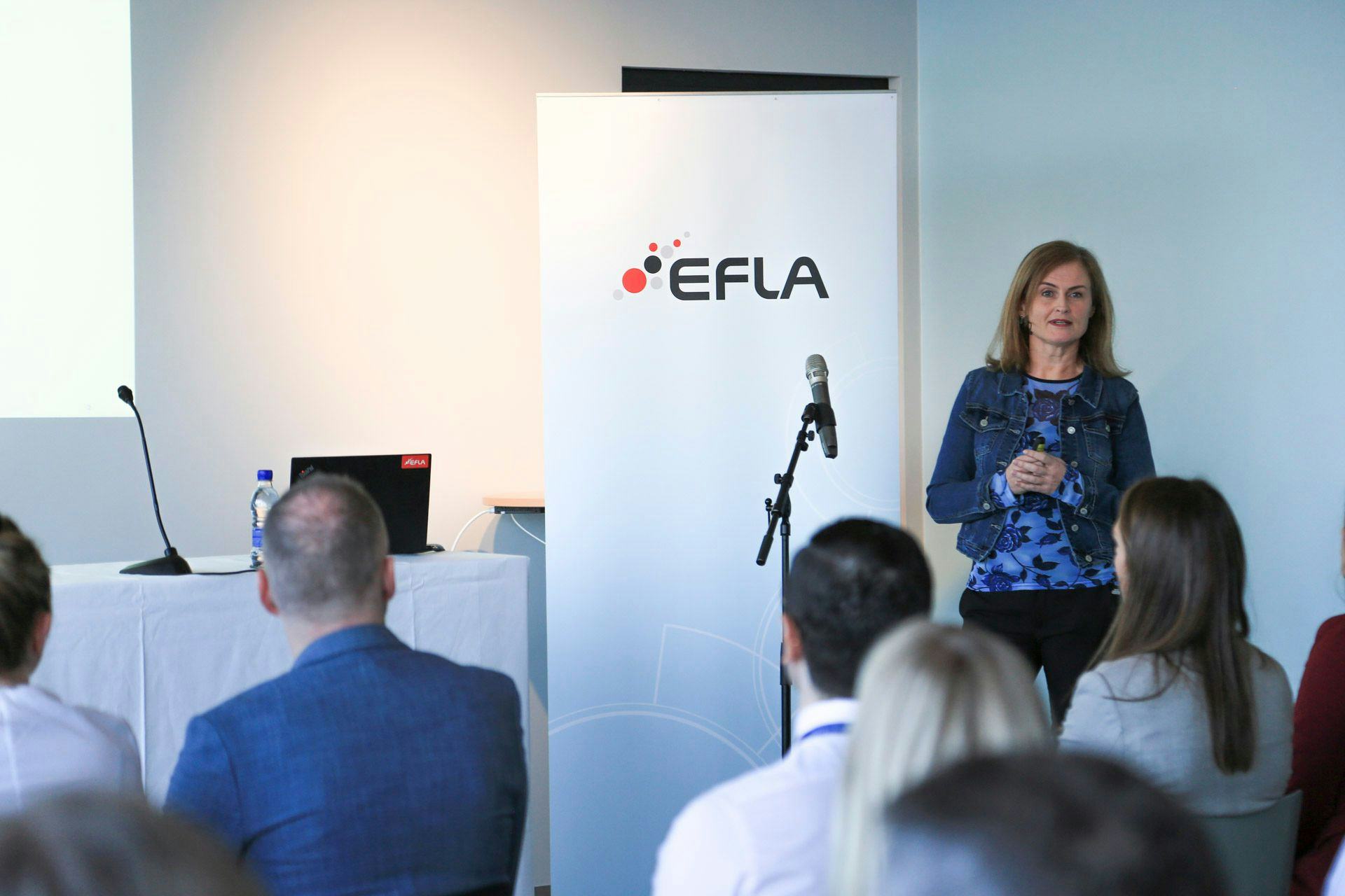 An audience listening to a speaker at a conference or presentation with the "EFLA" banner in the background