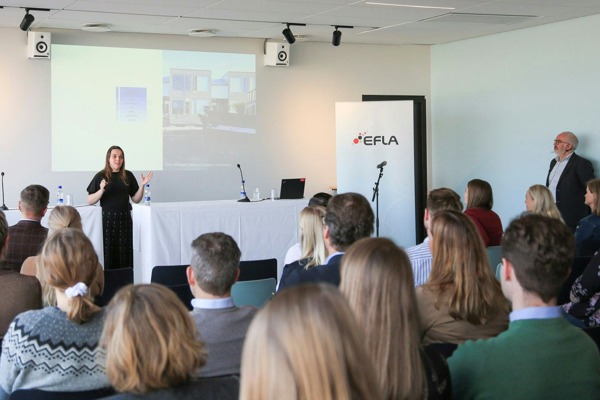An audience listening to a speaker at a conference or presentation with the "EFLA" banner and a big screen in the background