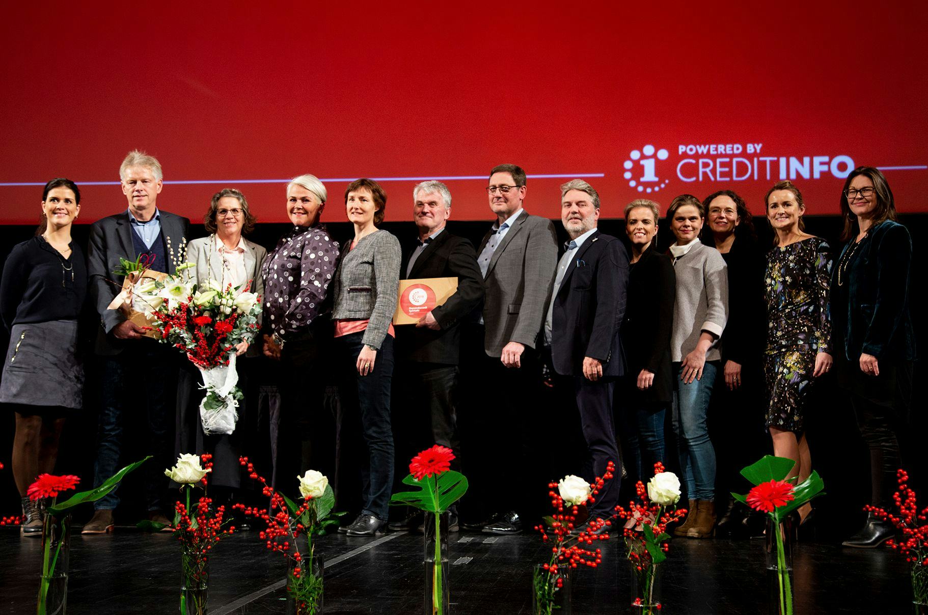 A group of people standing on a stage holding bouquet and certificate hosted by CreditInfo