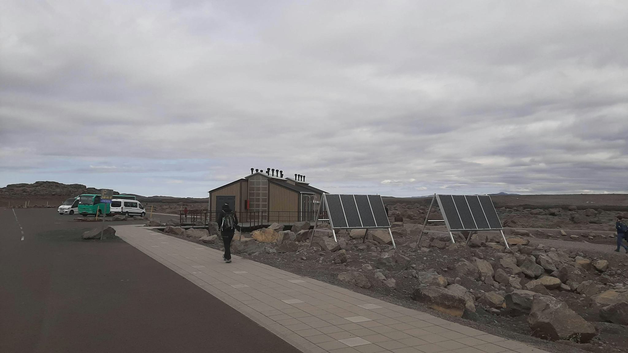 A person walking towards small cabin like structure with dark roof next to two solar cells
