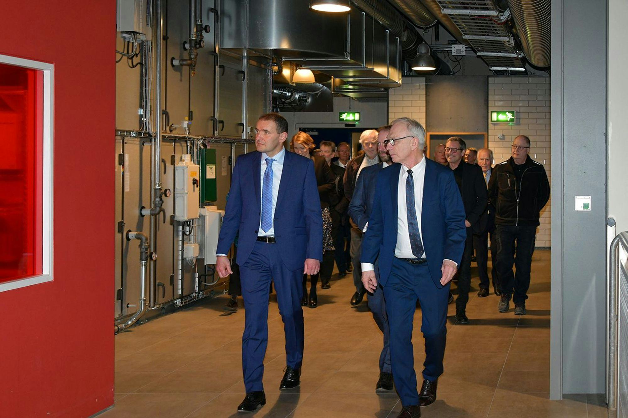Two men walking through an industrial setting with more people following behind them