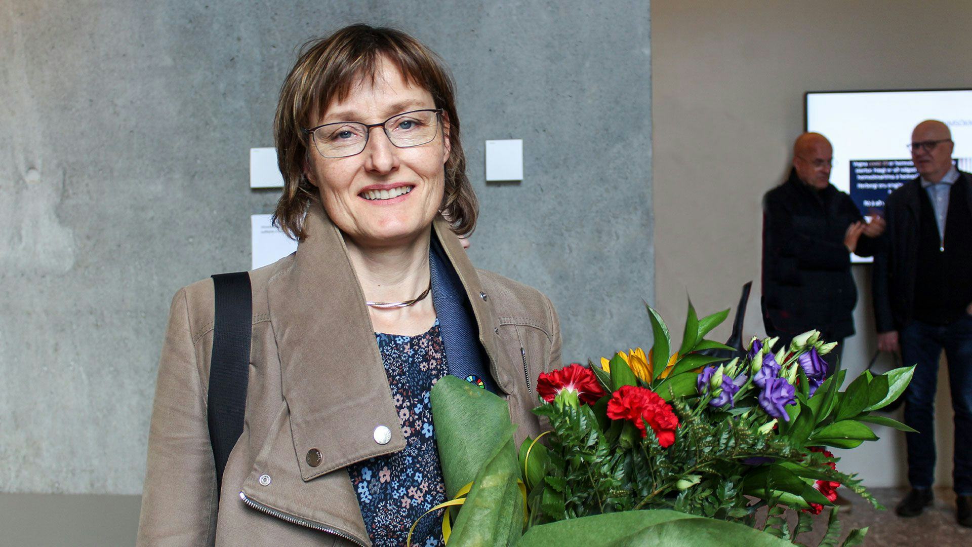A smiling woman in glasses holding a bouquet of flowers