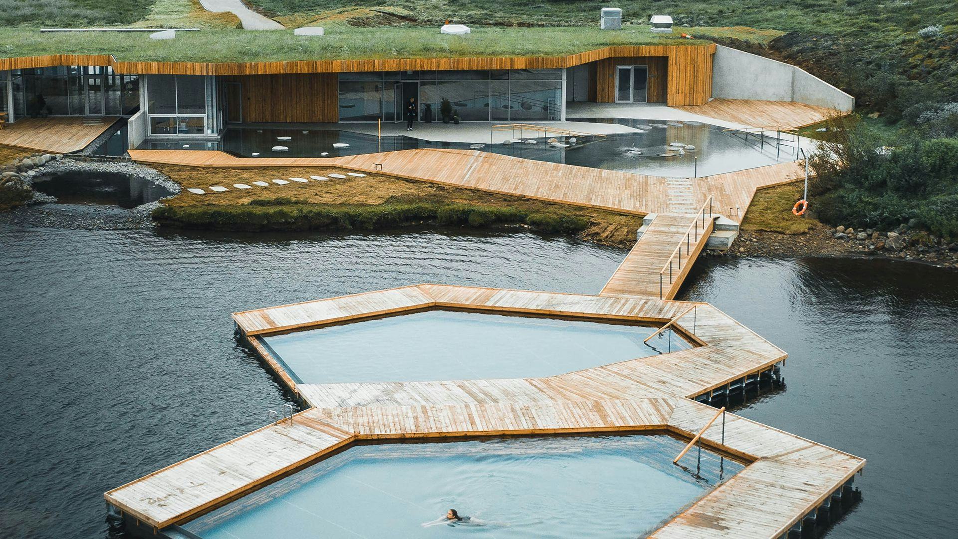 A modern geothermal bath featuring wooden walkways and pools over a body of water